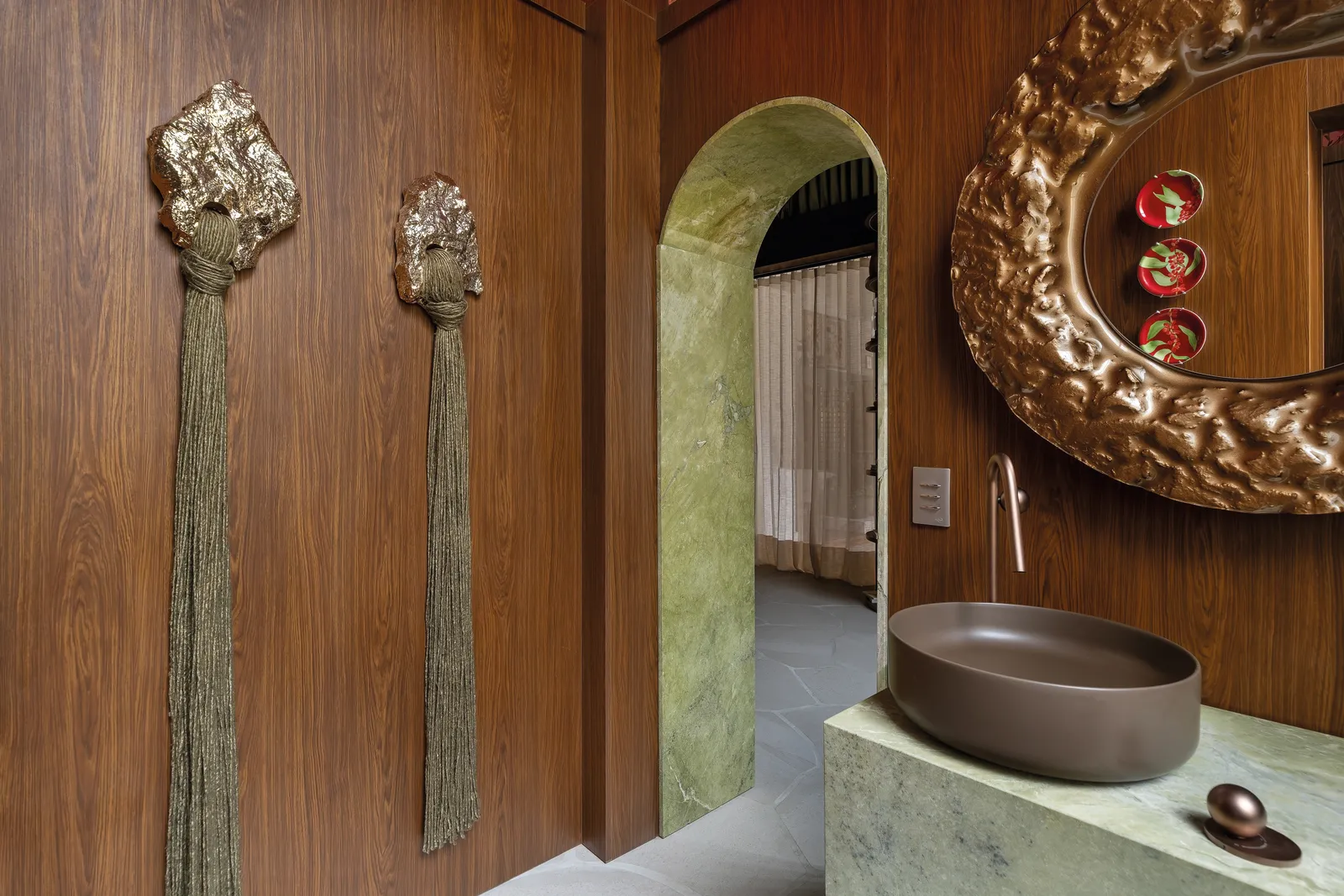 No lavabo projetado por Lucas, a cuba em tom marrom fosco faz uma composição interessante com as paredes em madeira escura, com a torneira e o espelho metalizados | Foto: Daniela Magario