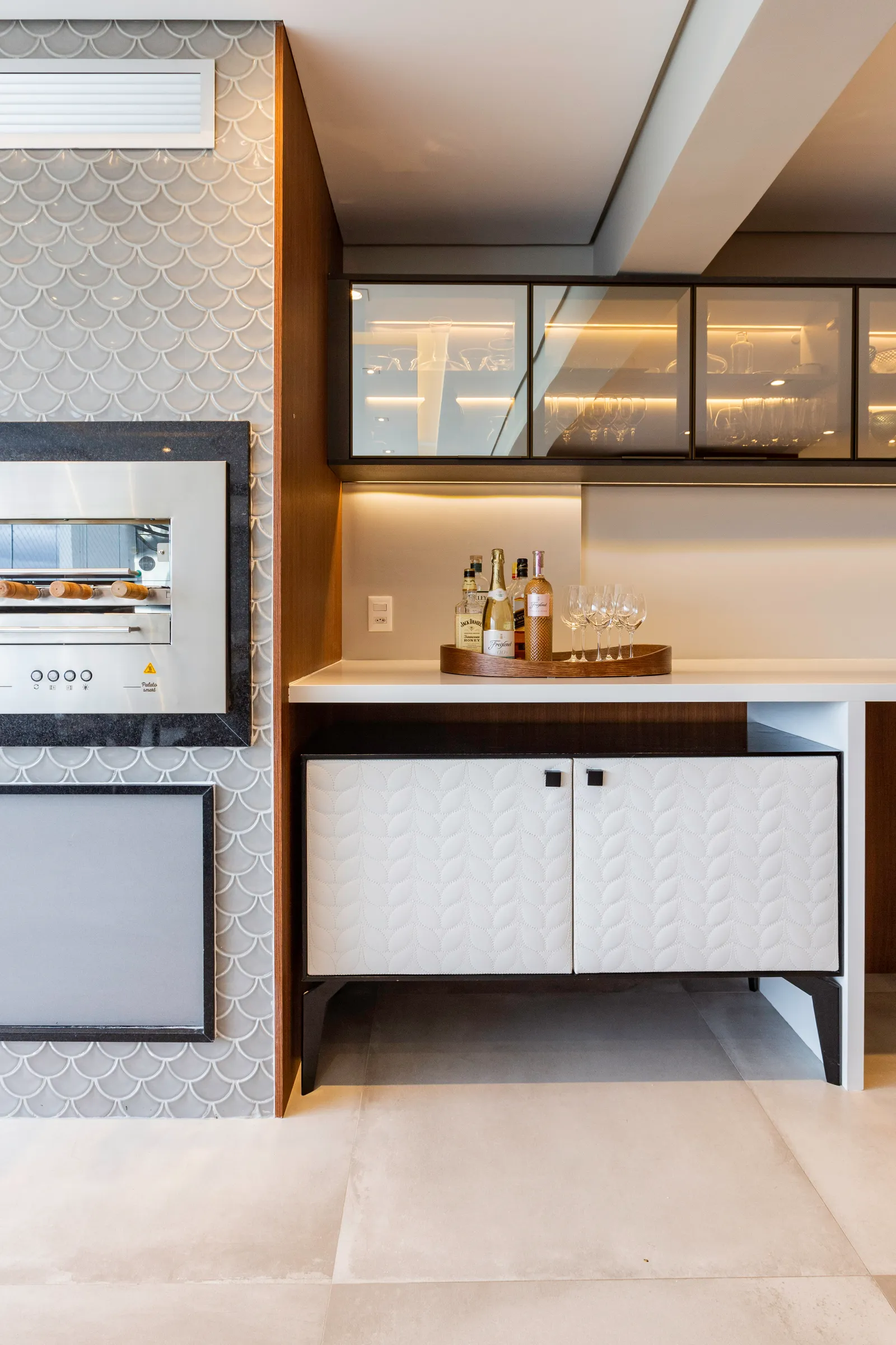 Na área social integrada deste apartamento, a cristaleira desenhada pela arquiteta Daniela Funari ocupa uma posição estratégica, uma vez que está disposta entre a sala de jantar e a varanda gourmet. Para complementar o efeito champagne do vidro, a iluminação interna facilita a visualização das taças e copos a serem escolhidas | FOTO: Mariana Camargo