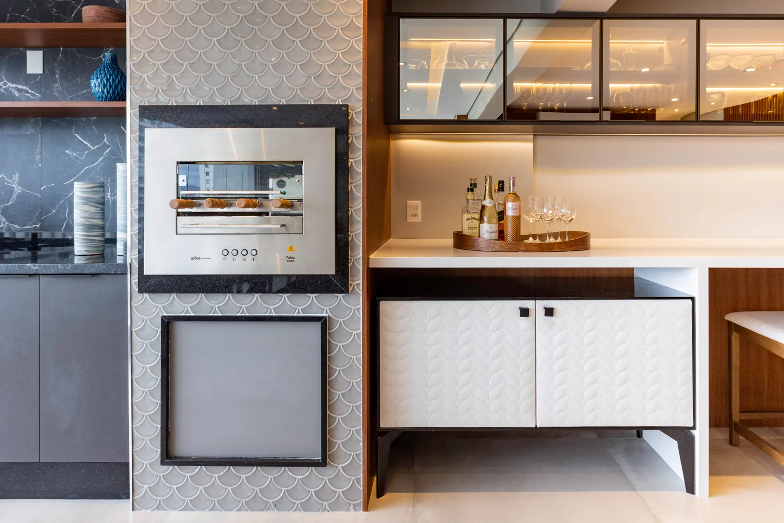 Na área social integrada deste apartamento, a cristaleira desenhada pela arquiteta Daniela Funari ocupa uma posição estratégica, uma vez que está disposta entre a sala de jantar e a varanda gourmet. Para complementar o efeito champagne do vidro, a iluminação interna facilita a visualização das taças e copos a serem escolhidas | FOTO: Mariana Camargo