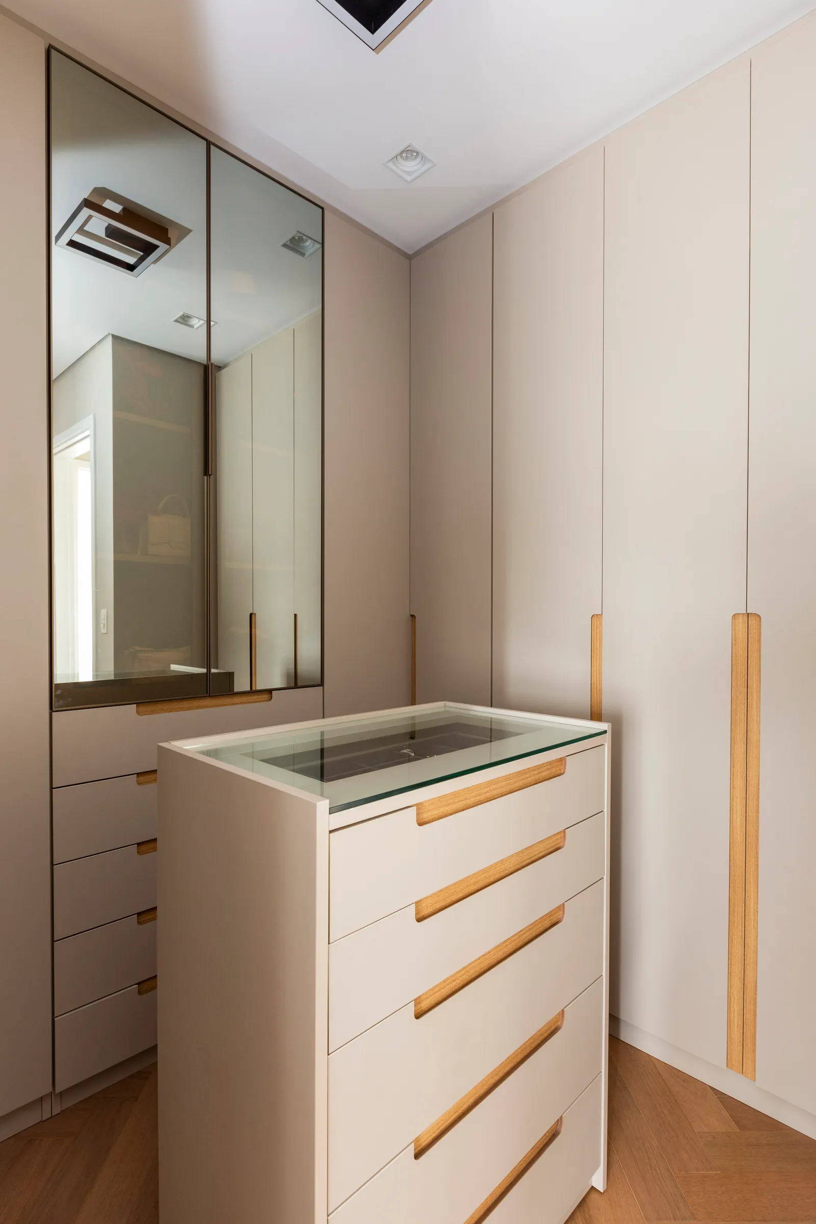 Para este closet walk-in, a arquiteta Daniela Funari trouxe apenas uma abertura central e o tampo da cômoda com o vidro reflecta, enquanto todo o restante do setor foi executado em marcenaria. “A ideia foi apresentá-lo como um ponto focal”, diz | FOTOS: Mariana Camargo