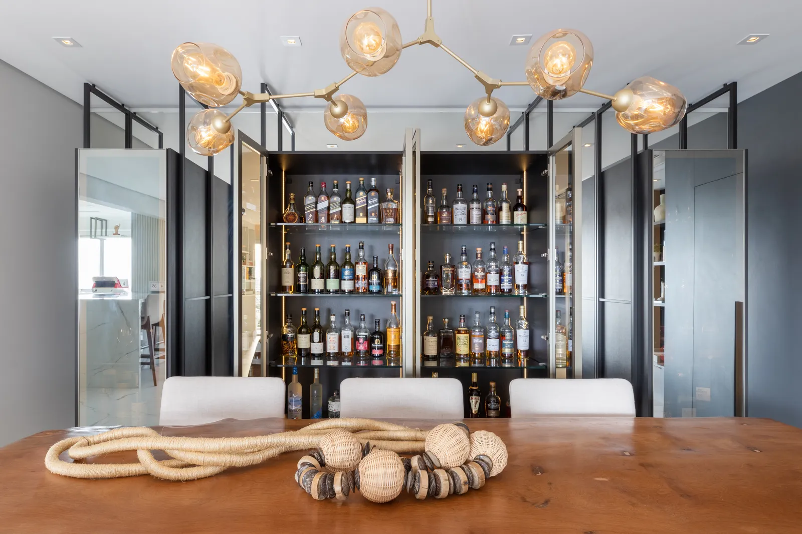 Na marcenaria que a arquiteta Daniela Funari realizou para esta sala de jantar, o vidro reflecta foi escolhido para as portas do móvel que guarda a coleção de whiskies dos proprietários. Contemporânea, a peça é estruturada com a serralheria que compreende a altura do piso ao teto | FOTOS: Julia Novoa