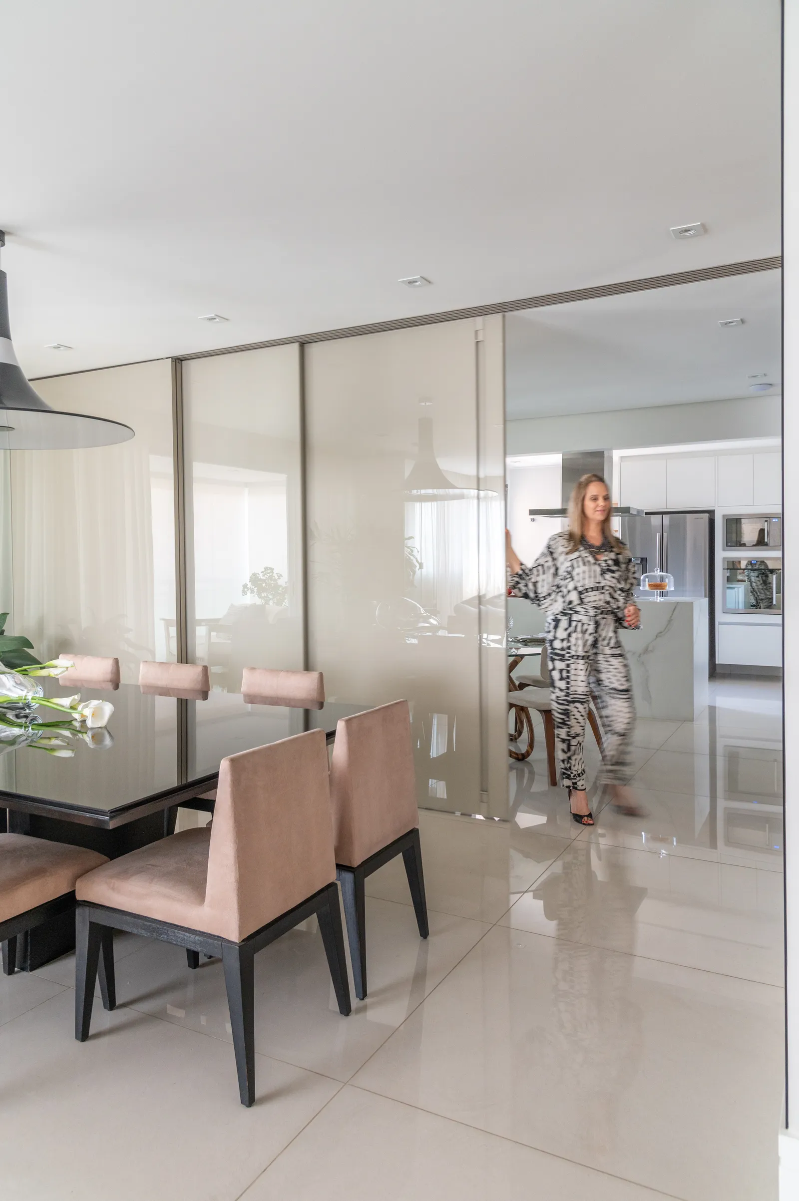 De vidro, está porta de correr separa a sala de jantar dos demais ambientes e bloqueia a entrada de luz, em que o material  é pintado e colado sobre um MDF laqueado da mesma cor, enquanto o sistema de trilhos reforça a leveza da medida adotada  pela arquiteta Isabella Nalon