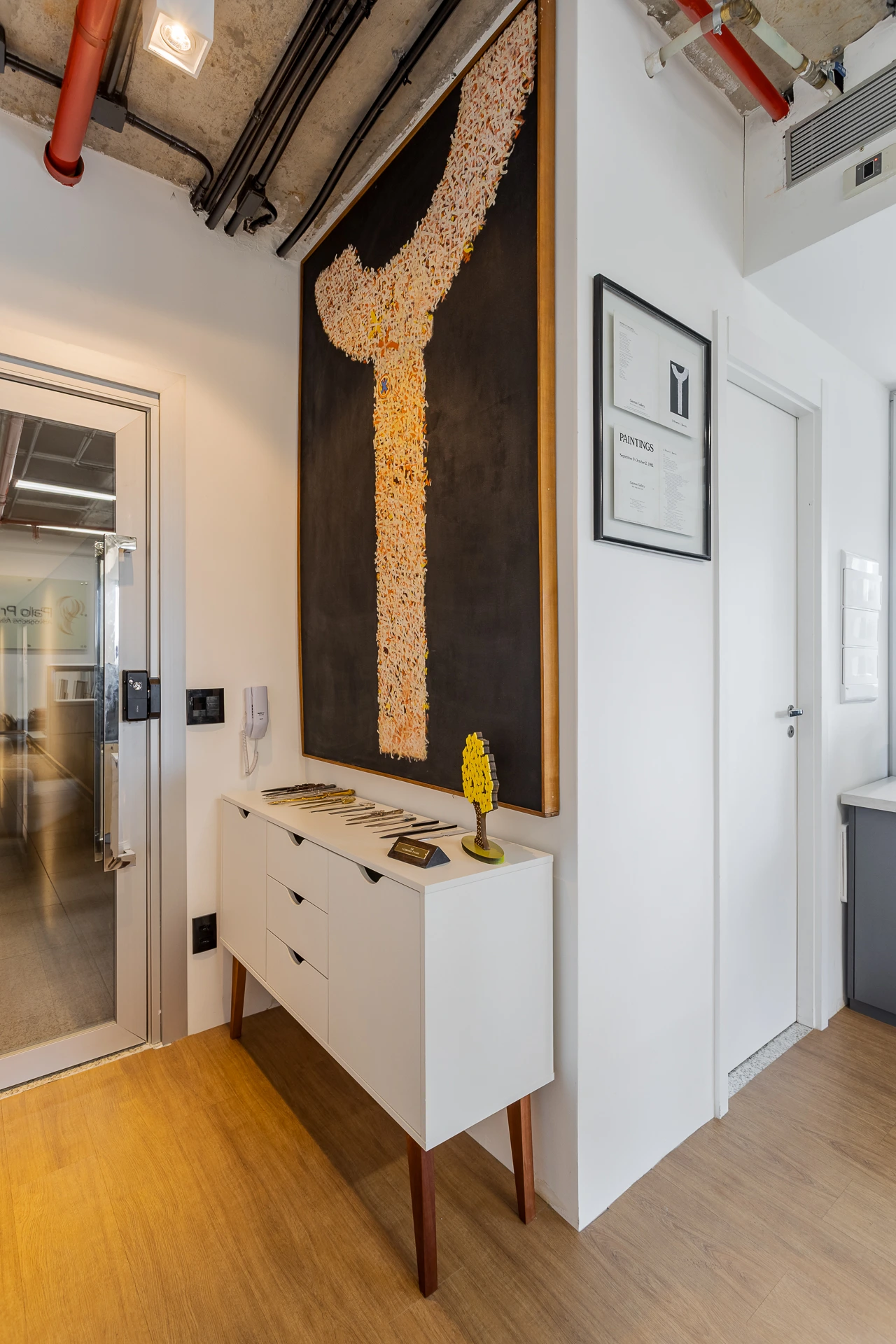 Projeto Camila Palladino | Ambiente de escritório com mesa de reunião em madeira, cadeiras estofadas e uma parede com revestimento texturizado, transmitindo elegância e conforto.