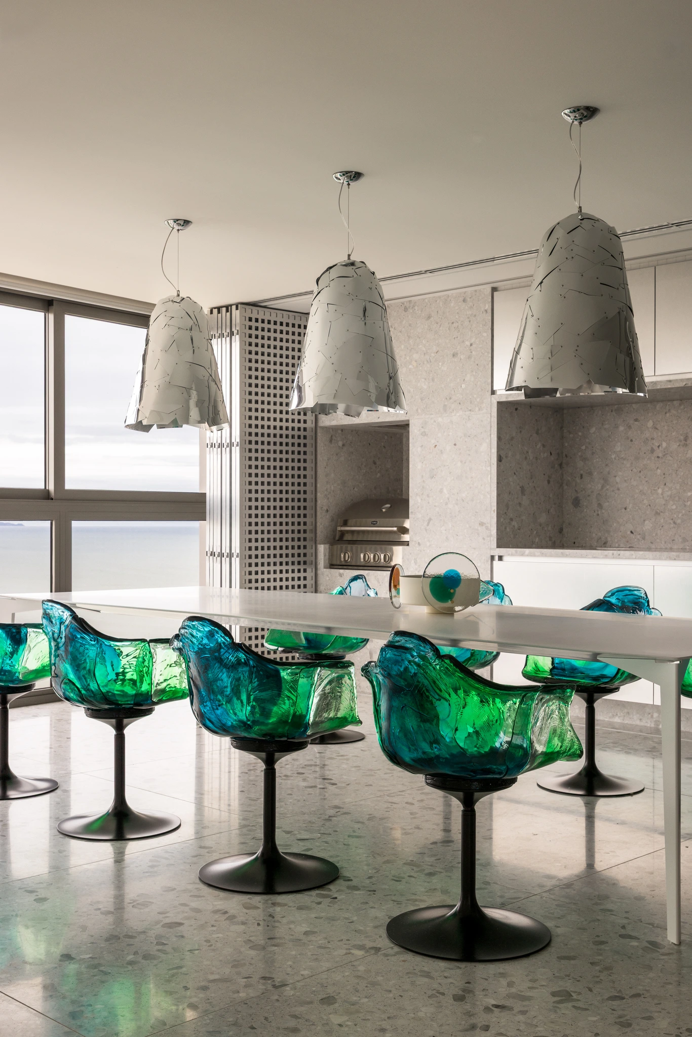Projeto: Paola Granzotto | Detalhe da sala de jantar com mesa em laca branca e cadeiras Ella de Jacopo Foggini, com pendente dos Irmãos Campana e vista para o mar.