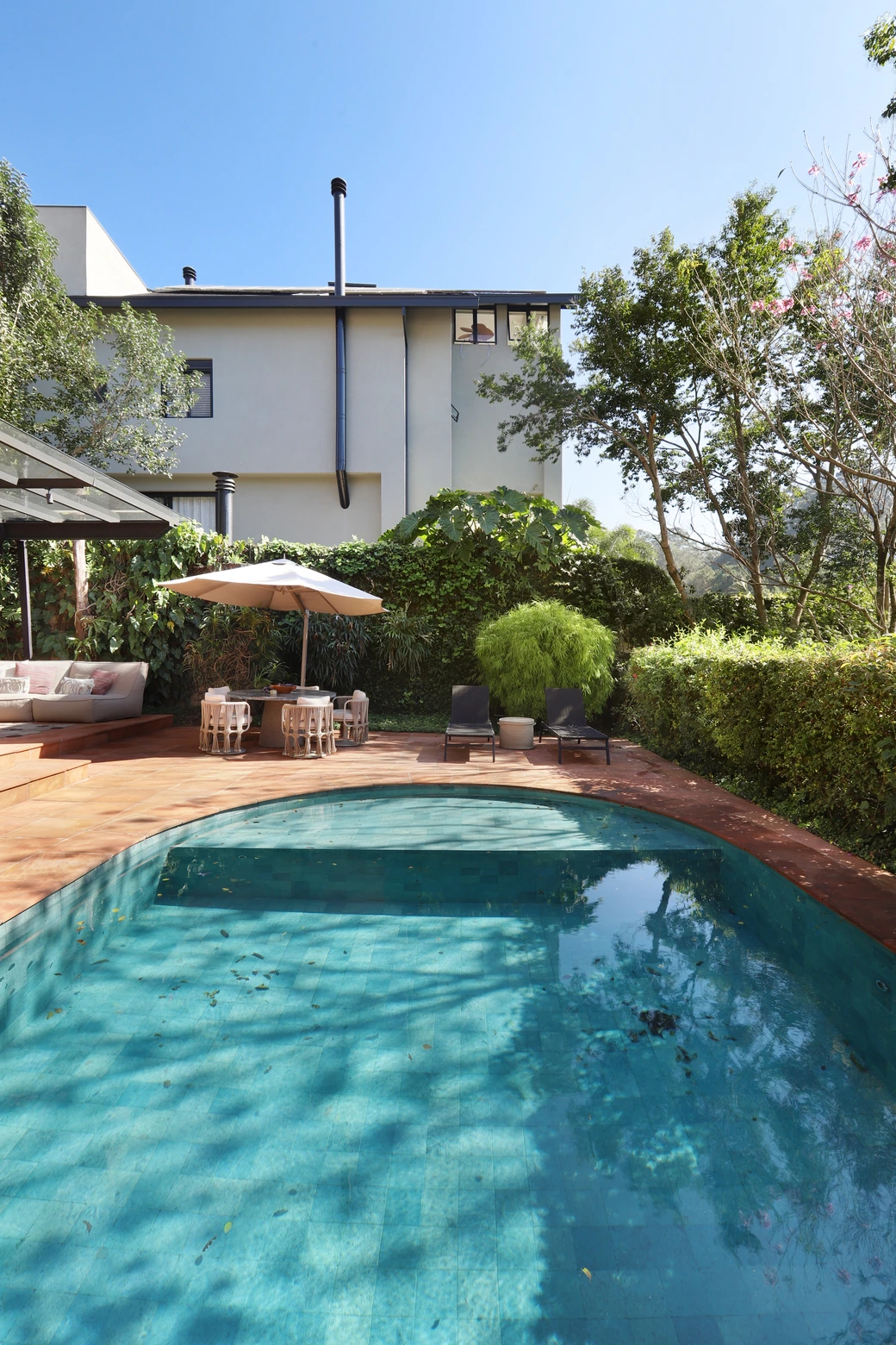 Vista da área externa da casa, com piscina e vegetação abundante, mobiliário da Tidelli e espreguiçadeiras.